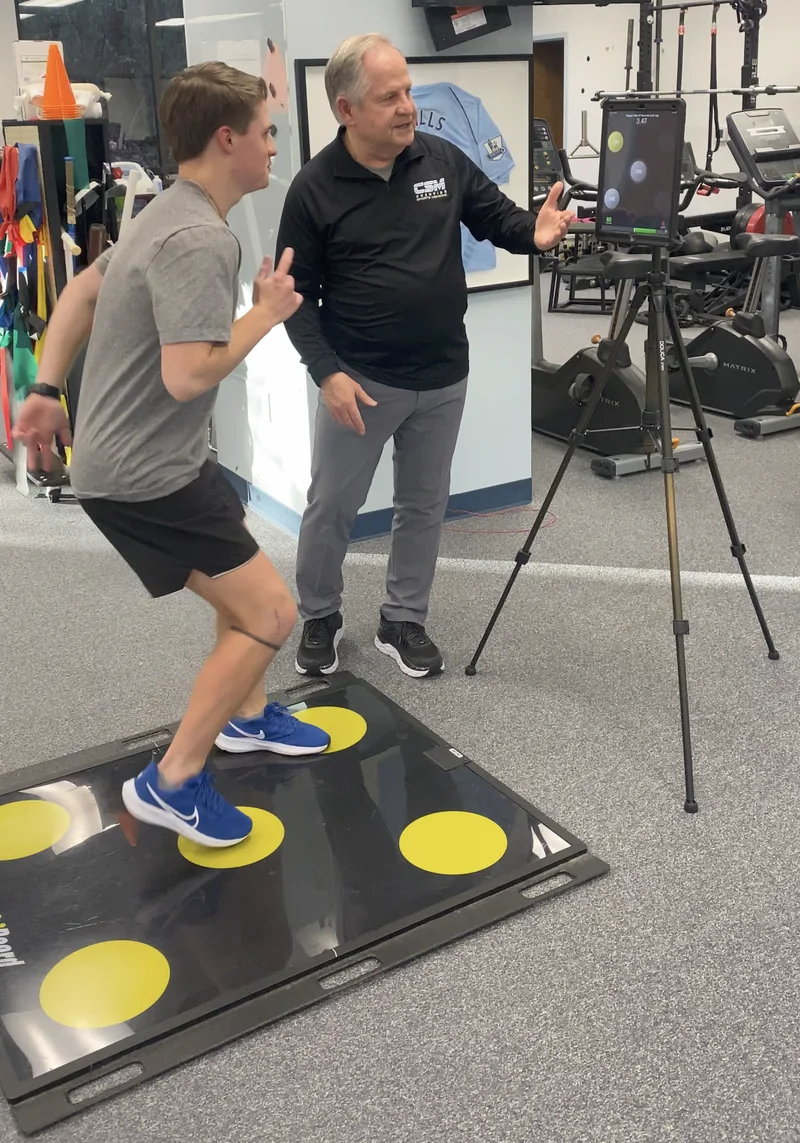 Clinician coaches an athlete through a reactive stepping drill on the QuickBoard sensor board, with live reaction times shown on the iPad